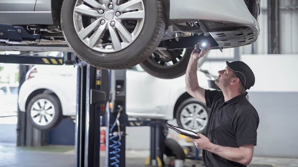 An LEC technician inspecting the underside of an electric car on a lift